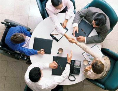Overhead picture of a group of people at a meeting table, including a person seated in a wheelchair.