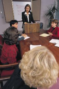 woman at podium at end of table speaking to a crowd