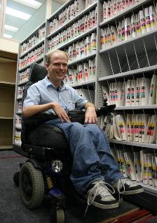 Man in powered wheelchair in front of stack of medical records.